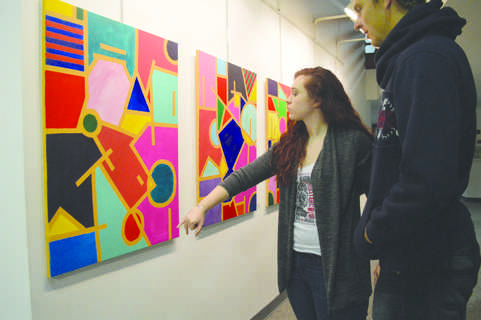 Sophomore theatre major Jordan Watson views artwork by senior visual arts major Laken Long during the “Color Talks” Senior Showcase. Long’s work featured colorful paintings with geometric patterns. In the future, Long hopes to transform her paintings into fashion designs to be printed on clothing.